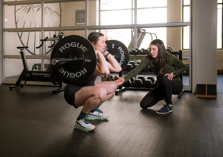 A Steady State physical therapist coaching a client through a barbell squat.
