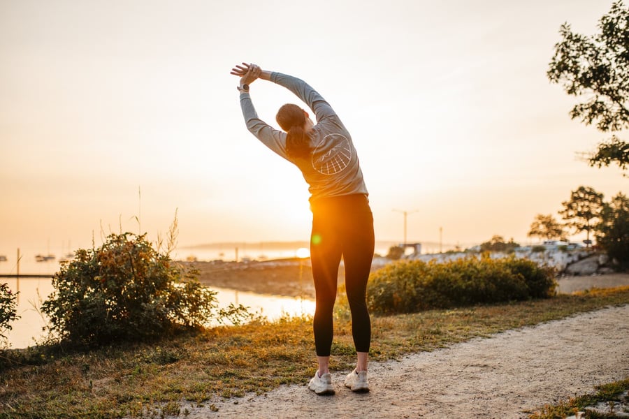 A runner stretching through her trunk at sunrise in Portland, Maine.
