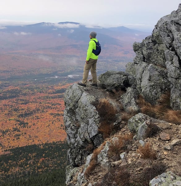 A Maine hiker pondering a view on the side of a cliff.